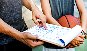 coach holding a clip board with basketball plays on it 