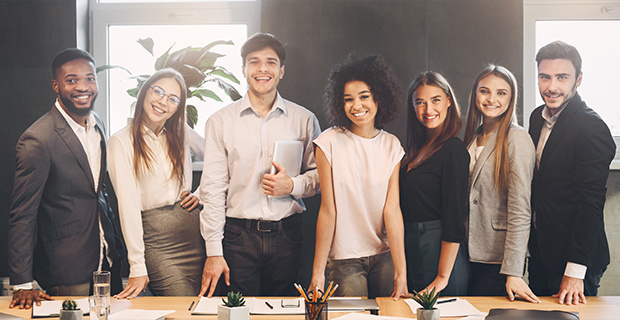 A diverse group of young professionals, including men and women, standing together in an office setting