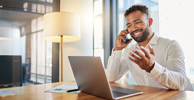 Businessman smiling while on a cell phone and working on a laptop